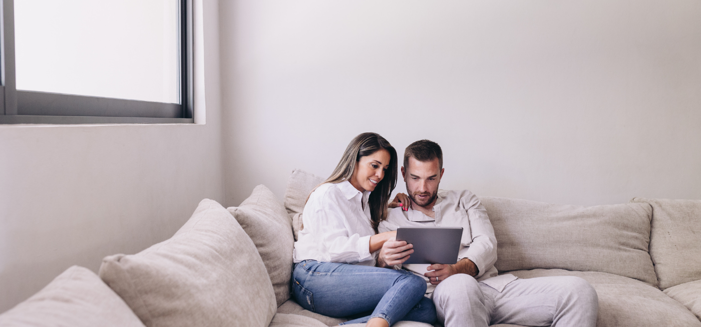 Casal sentado no sofá a consultar um tablet em conjunto